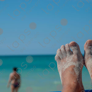 Brown feet in sand, turquoise sea in the background