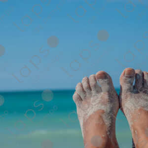 Feet with tan skin covered in sand, with a background of turquoise sea