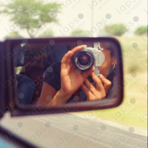 Reflection of the photographer with an old camera in the rearview mirror