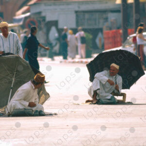 Two Men in Traditional Attire Sitting with Umbrella at Jemaa el-Fna Square, Marrakech